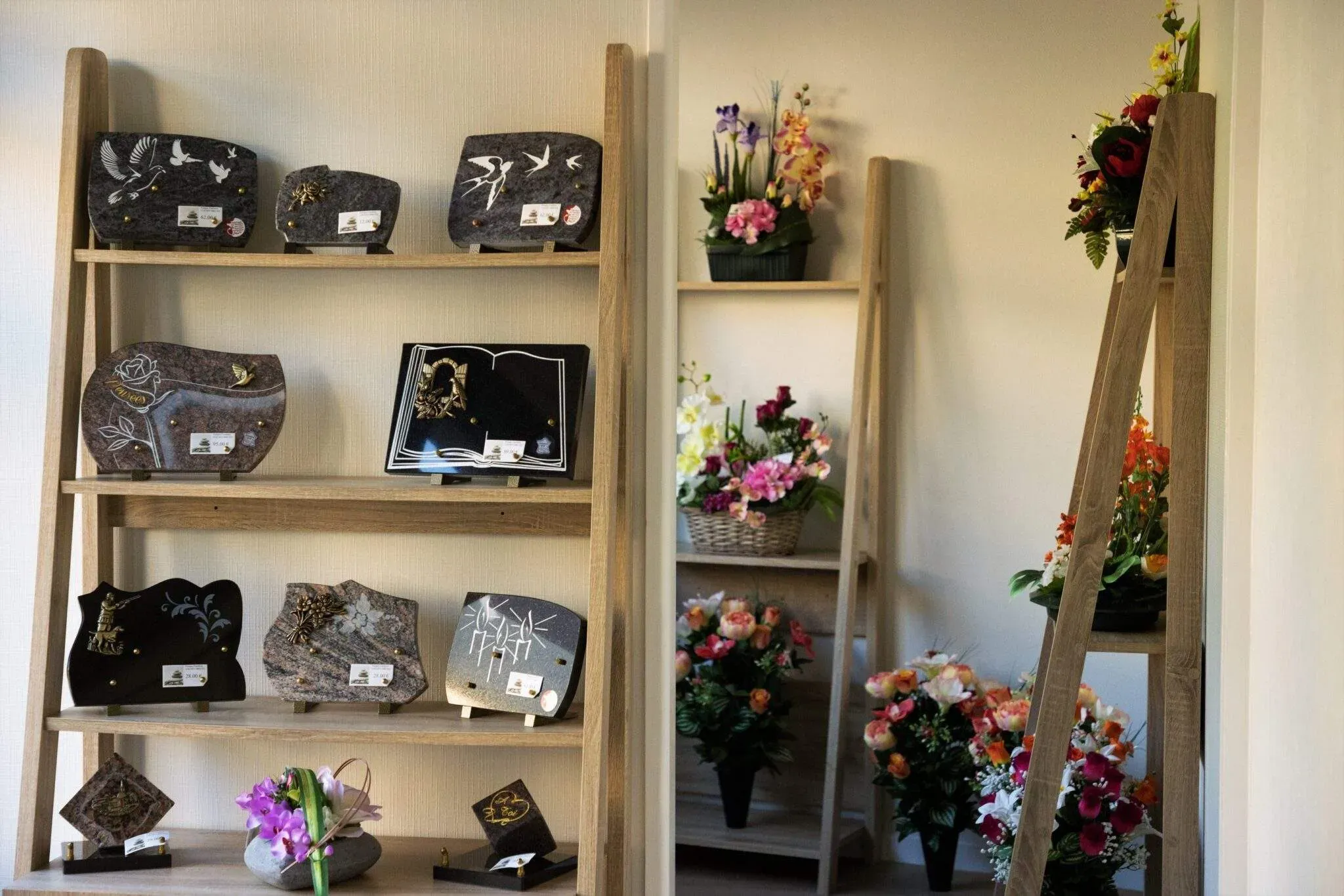 Plaques funéraires personnalisées et bouquets de fleurs exposés sur des étagères.