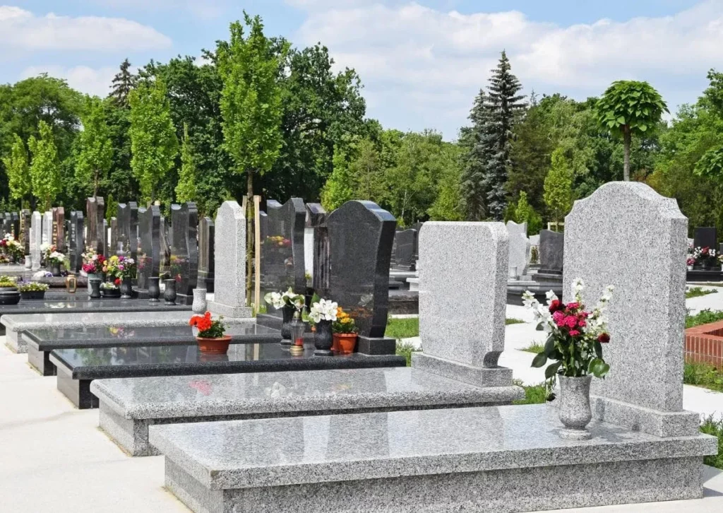 Alignement de monuments funéraires en granit et tombes fleuries dans un cimetière.